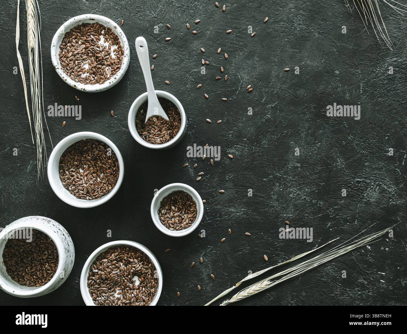 Graines de lin et épi de seigle sec sur fond sombre. Ensemble de petits bols avec graines de lin bio ou graines de lin. Les graines de lin sont riches en acides gras oméga-3. Copier Banque D'Images