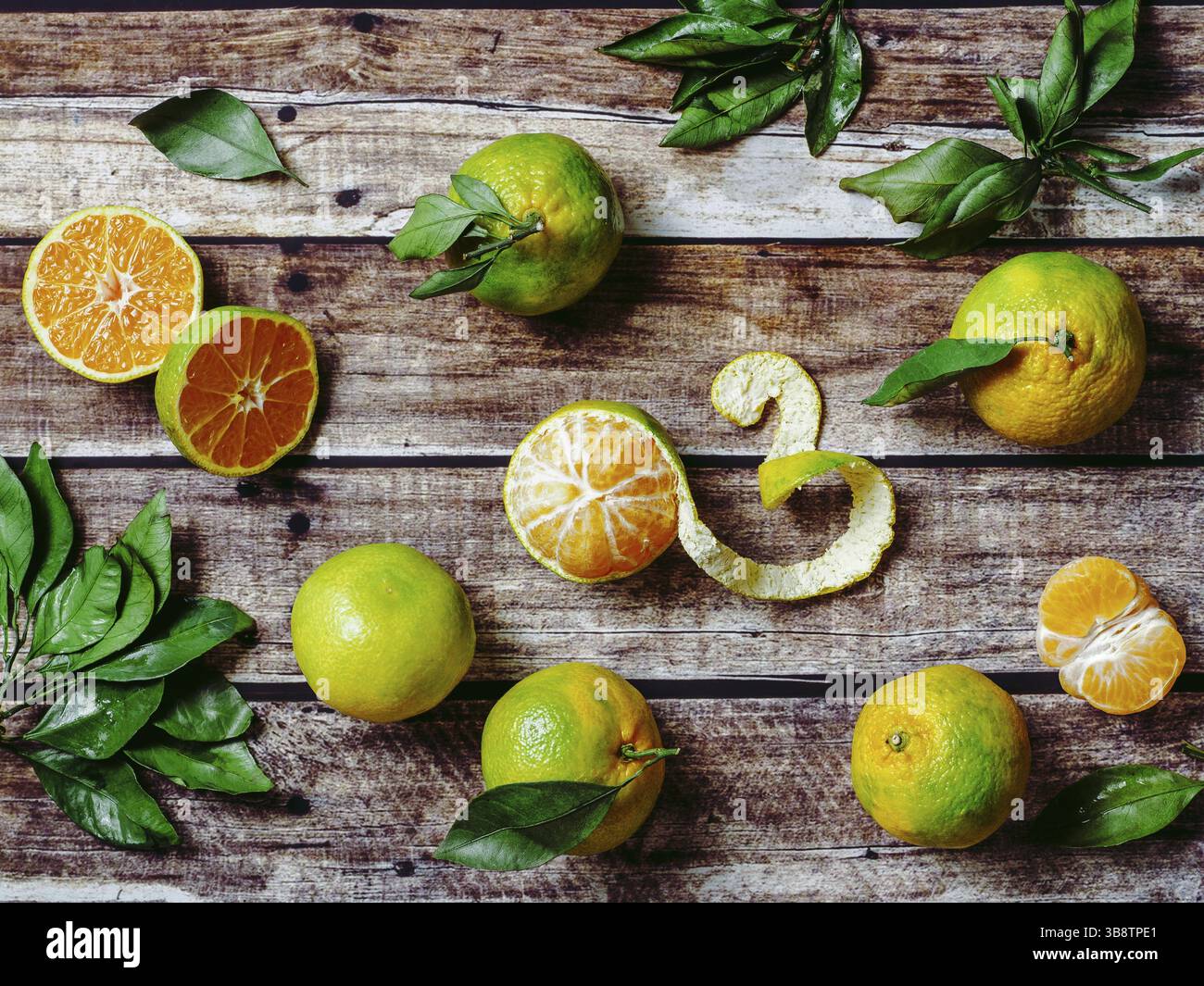 Mandarines vertes sur fond de bois ancien. Demi-mandarines fraîches et mûres, entières et pelées, avec feuilles, vue de dessus ou à plat Banque D'Images