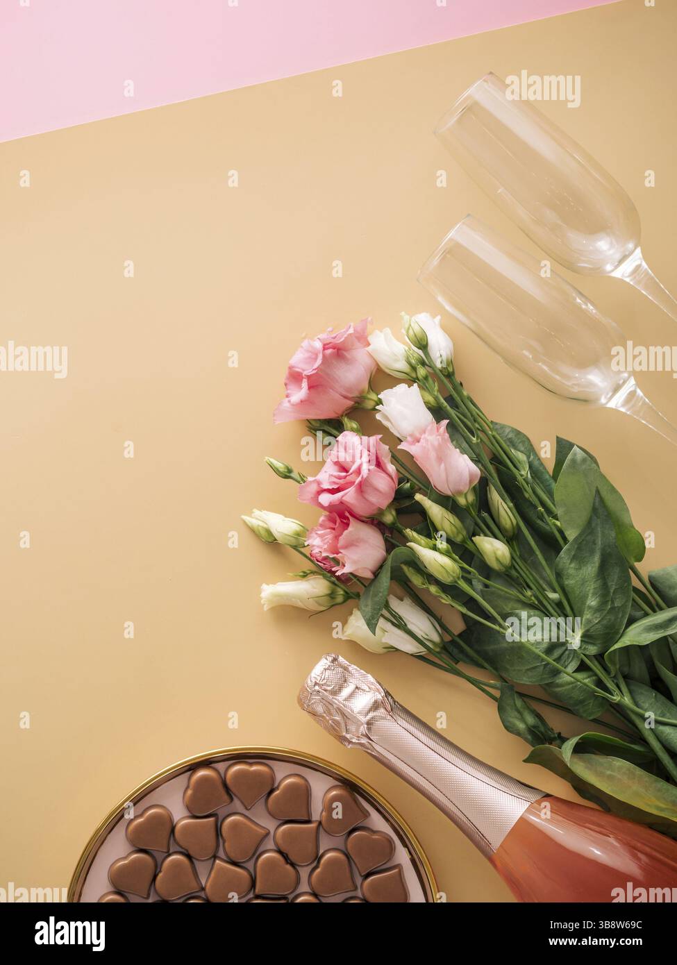 Concept de Saint-Valentin sur fond jaune pastel. Bouteille de champagne rose, verres, bouqet de fleurs et confiseries romantiques au chocolat en forme de coeur. Banque D'Images