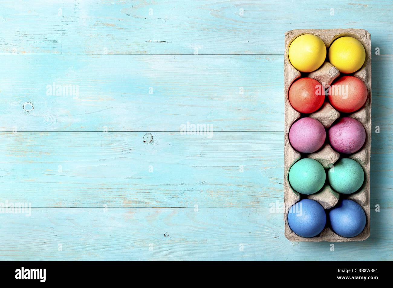 Concept de Pâques. Œufs colorés dans un emballage en carton sur fond bleu en bois avec espace de copie pour le texte. Vue de dessus ou plat Banque D'Images