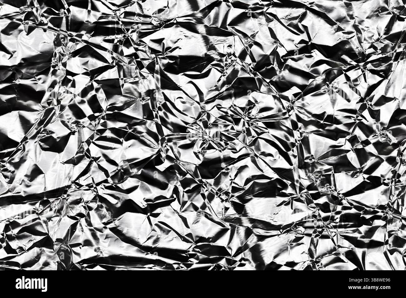 Texture de feuille plissée. Surface argentée brillante avec plis métalliques. Fond froissé avec des reflets lumineux. Gros plan sur le matériau d'emballage. Banque D'Images