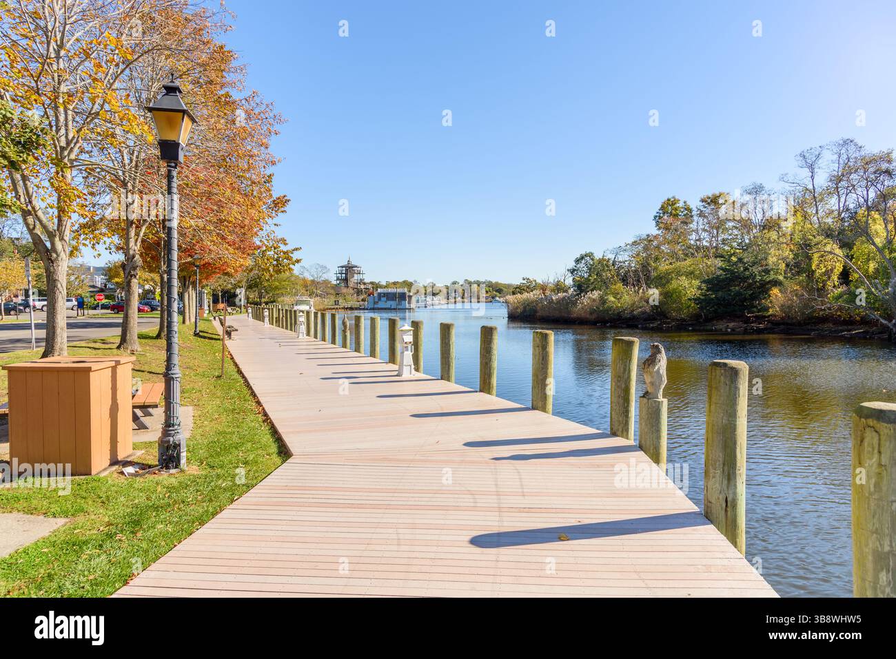 Promenade vide bordée d'arbres et de bancs en bois et lampadaires sur un port fluvial par un matin clair d'automne. Les bateaux amarrés sont visibles à distance. Banque D'Images