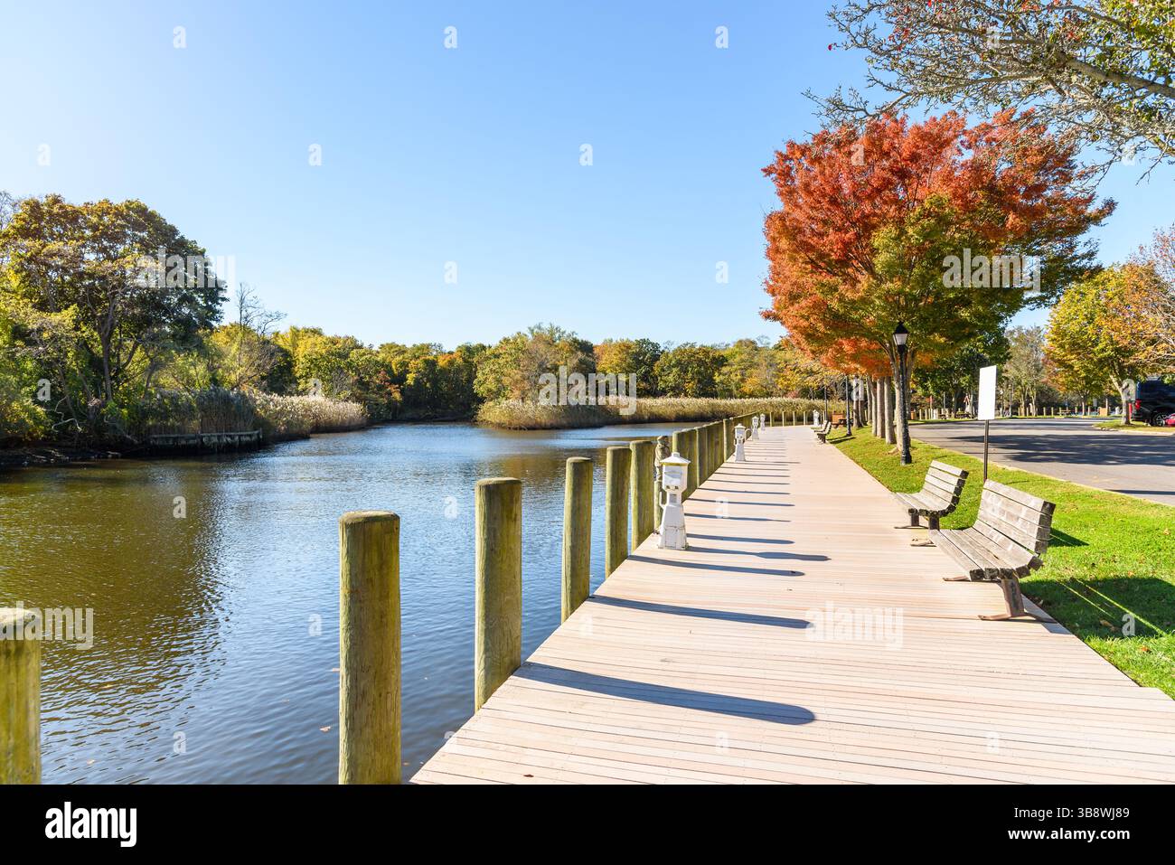 Promenade en bois déserte bordée de bancs et d'arbres colorés longeant une rivière par un clair jour d'automne Banque D'Images