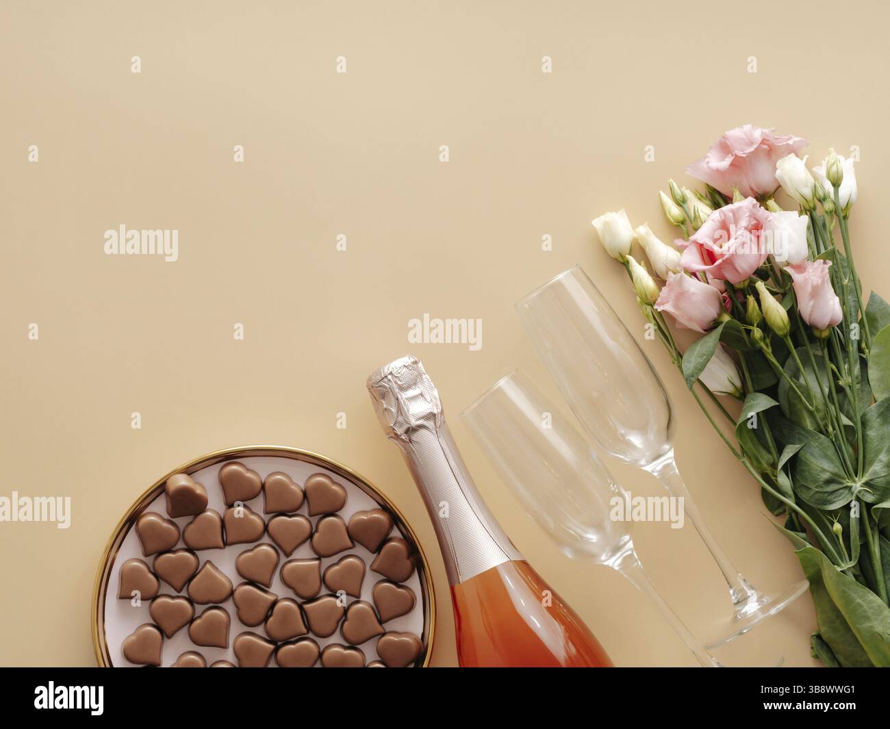 Concept de Saint-Valentin sur fond jaune pastel. Bouteille de champagne rose, verres, bouqet de fleurs et confiseries romantiques au chocolat en forme de coeur. Banque D'Images