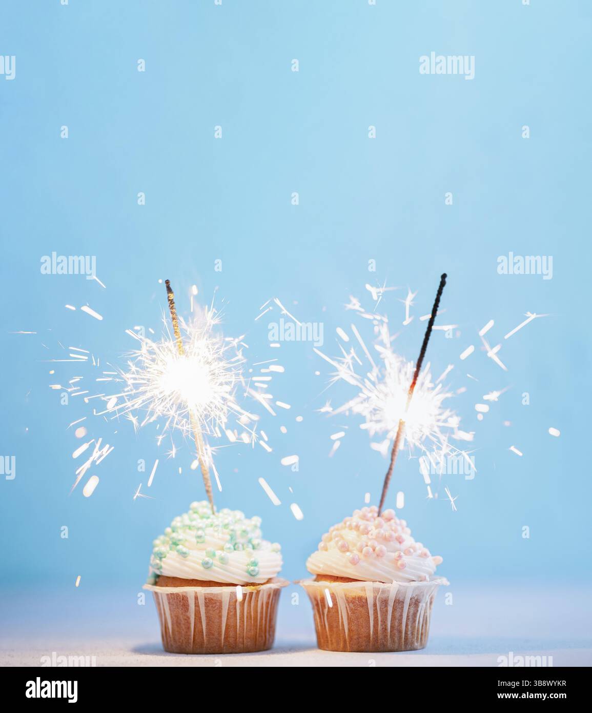 Deux cupcakes décorés de pépites colorées et de pétillants. Cupcakes festifs avec des saupoudrages bleus et roses sur fond bleu avec top d'espace de copie pour Banque D'Images