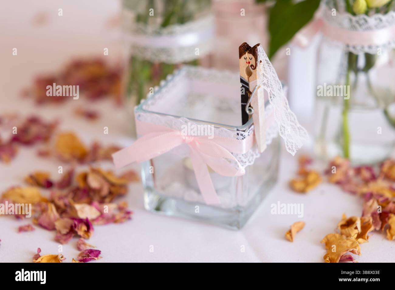 Embrasser épingle à linge toppers gâteau de mariage reposant sur un vase en verre décoré avec des pétales de rose dispersés autour d'une table de réception de mariage Banque D'Images