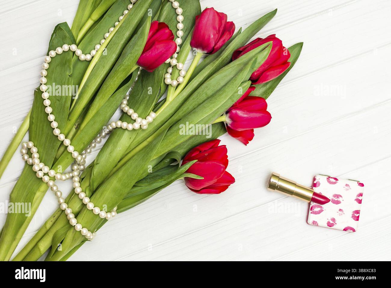 Vue de dessus beau bouquet de tulipes rouges dans le collier, rouge à lèvres sur fond de planche de bois blanc Banque D'Images