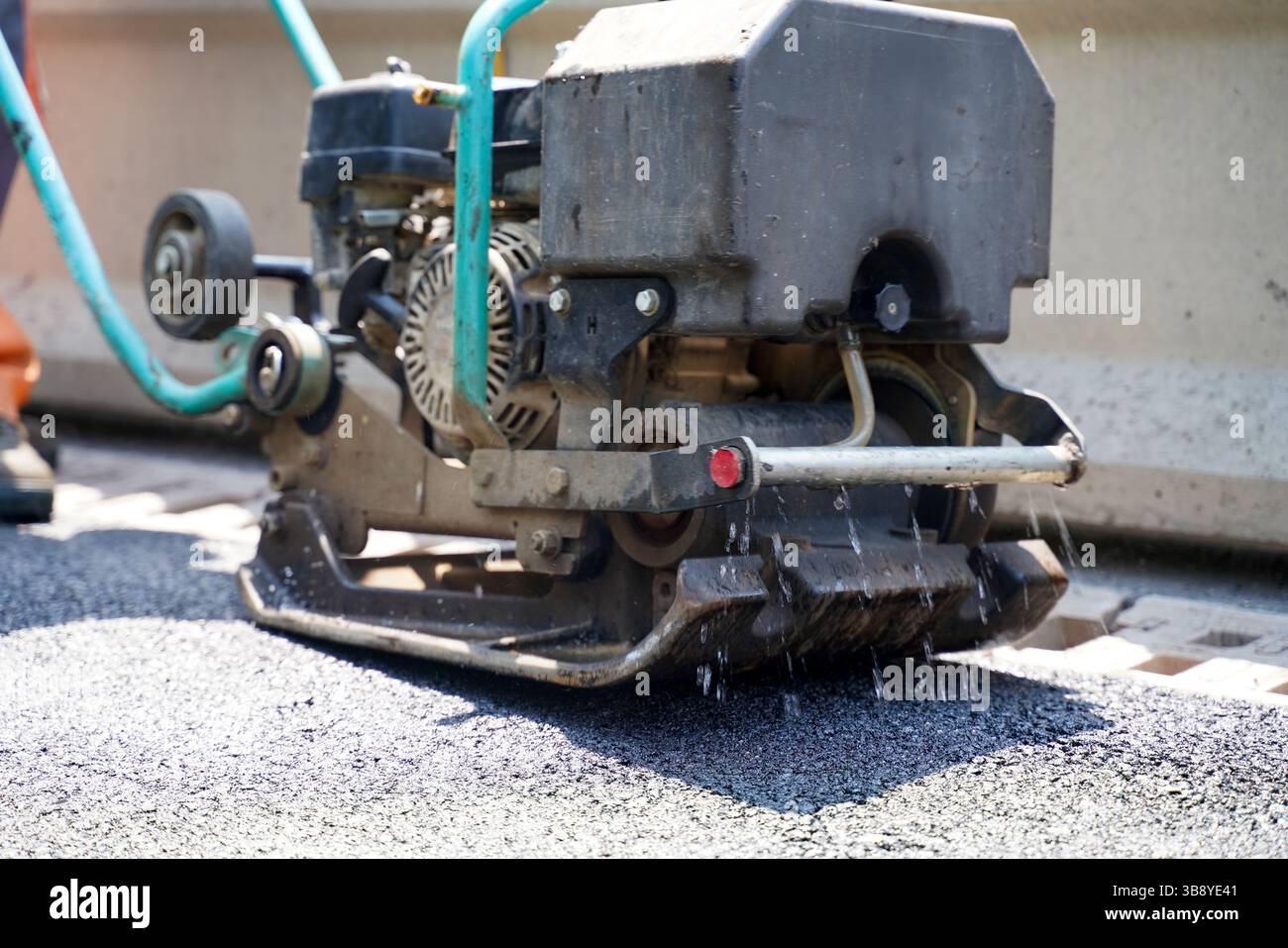 Gros plan d'une machine de construction à plaques vibrantes compactant de l'asphalte frais sur un chantier de construction d'autoroute. Banque D'Images