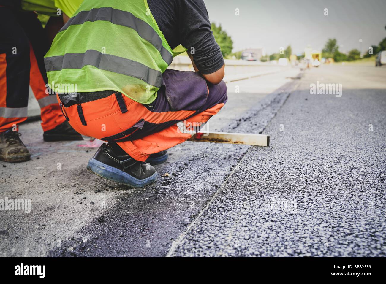 Travailleur de la construction mesurant l’asphalte frais pour s’assurer de son niveau, assurant précision et qualité pendant le processus de pavage routier sur un chantier de construction Banque D'Images