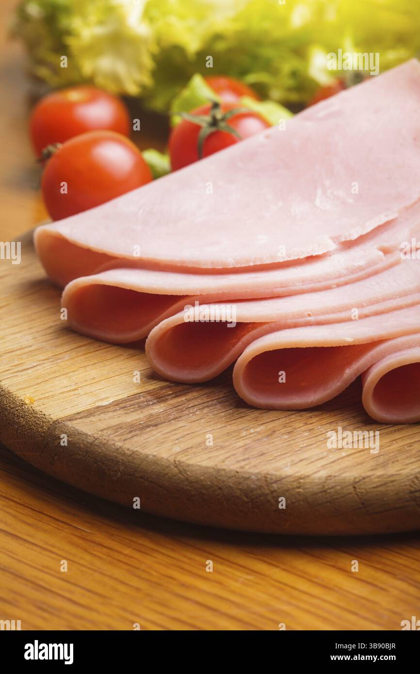 Tranches de jambon frais avec lattuce et tomate cerise sur la planche de bois Banque D'Images Tranches de jambon frais avec lattuce et tomate cerise sur la planche de bois Banque D'Images