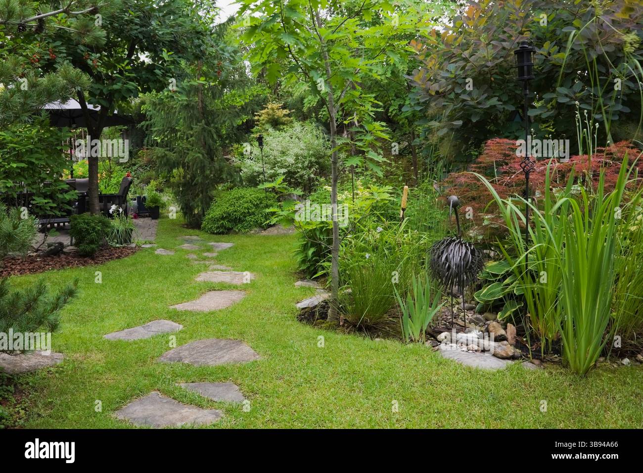 Chemin de dalles à travers le jardin arrière avec sculpture d'oiseau en métal et Prunus - Cherry, Pinus parviflora glauca - PIN blanc japonais, Quercus - chêne, AC Banque D'Images