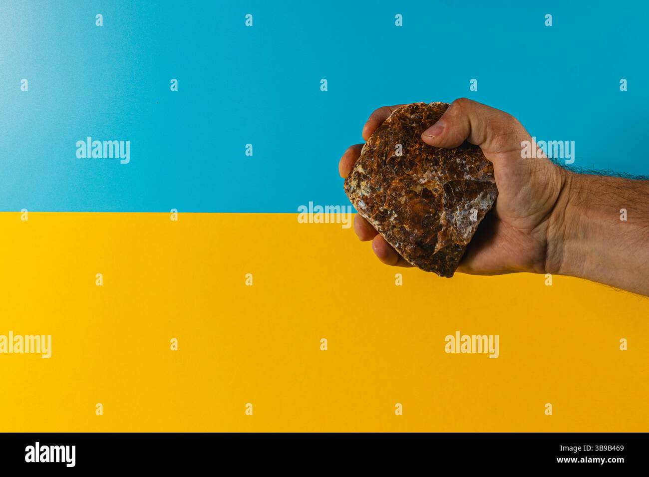 Une main saisit fermement une roche texturée tout en positionnant sur un fond bleu et jaune éclatant qui crée un contraste visuel saisissant pendant la journée Banque D'Images