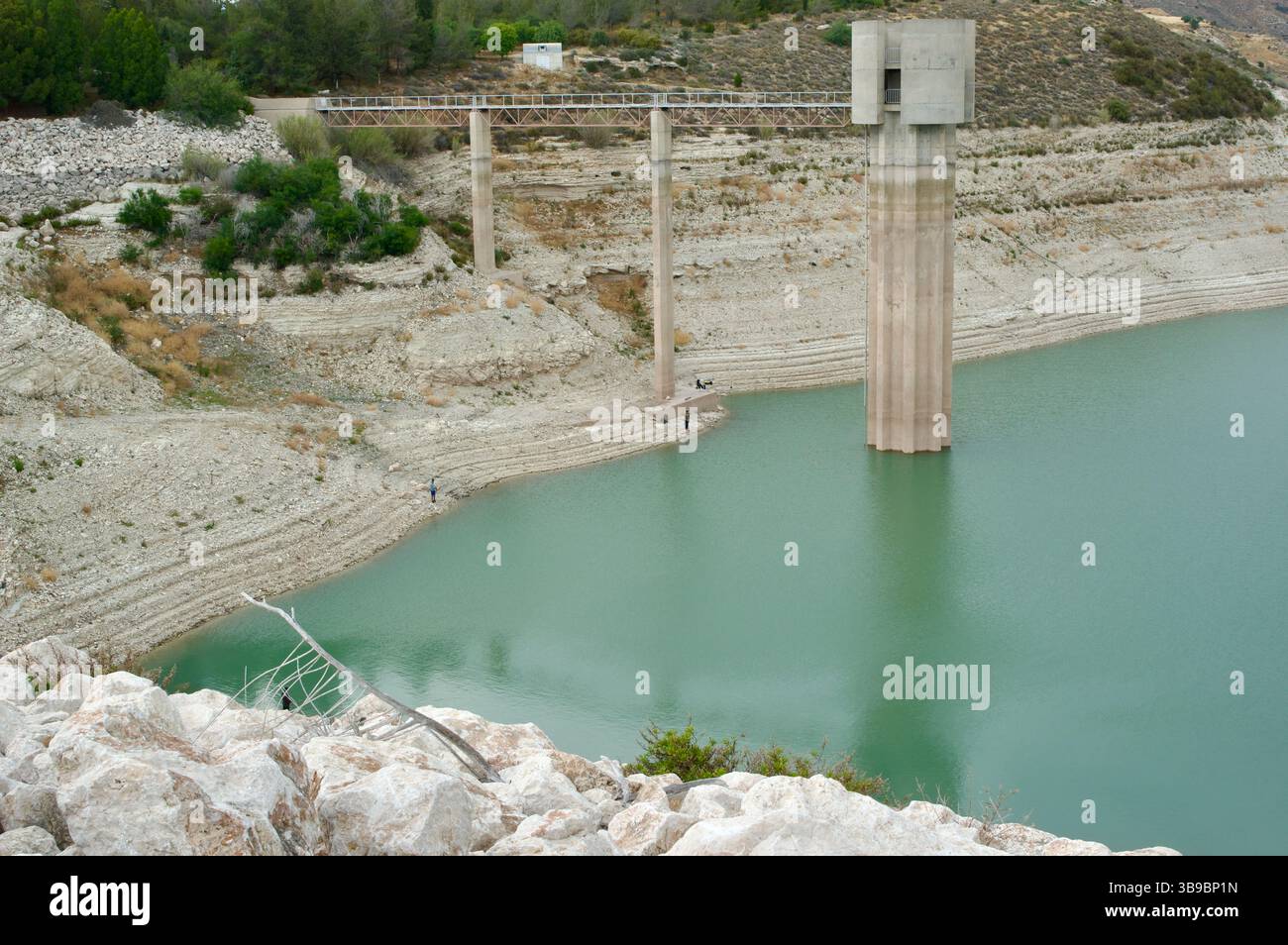 Un réservoir connaissant des conditions de sécheresse, montrant des niveaux d'eau bas et une structure hydraulique proéminente au milieu d'un paysage aride et sombre. Banque D'Images