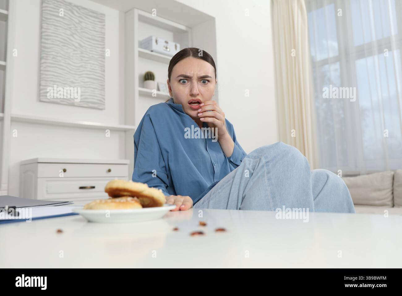 Jeune femme choquée regardant des cafards et des bretzels sur une table blanche à l'intérieur. Problème de ravageur Banque D'Images