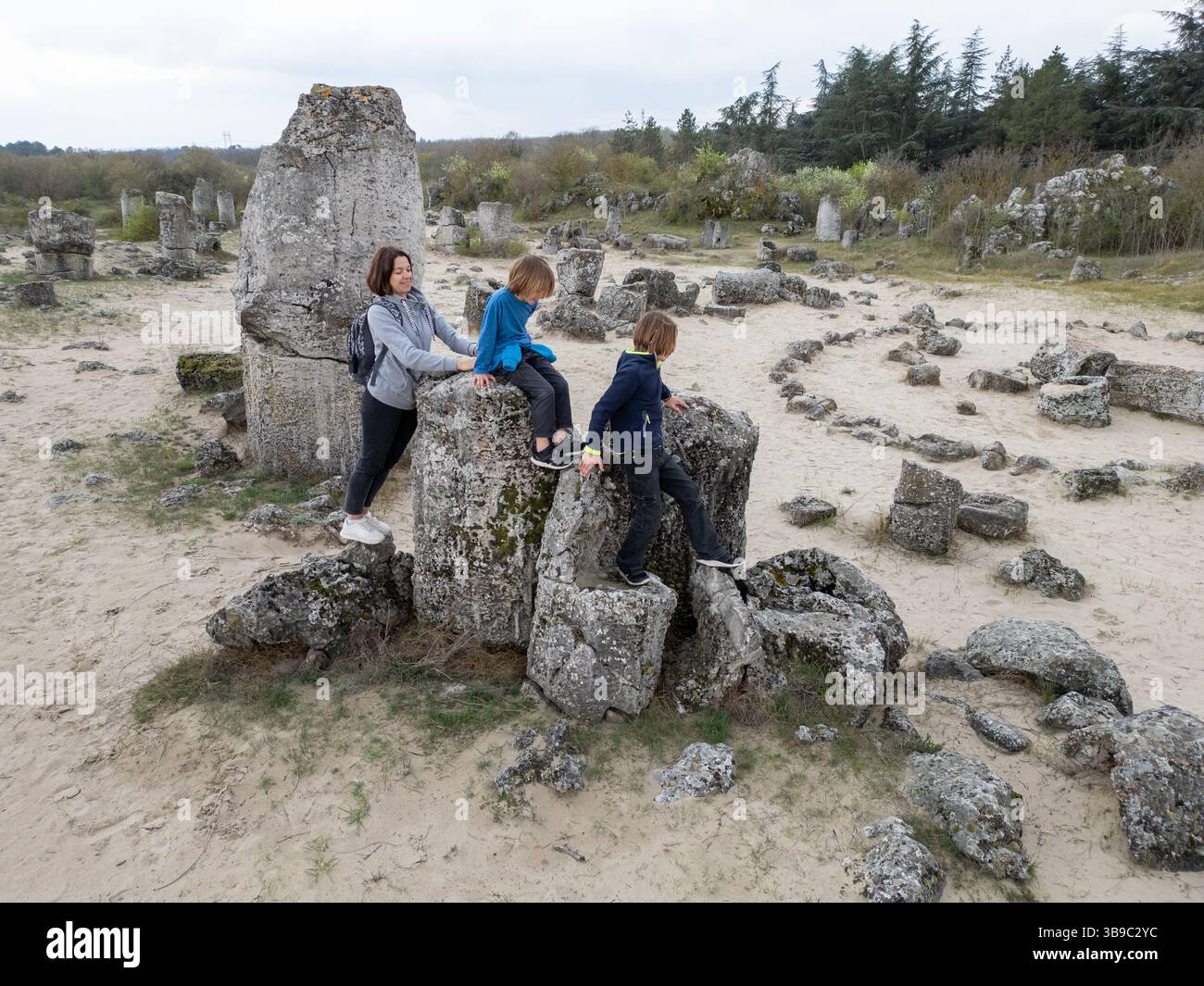 Mère et deux enfants explorent un terrain rocheux dans un paysage sec et semi-désertique. Les enfants jouent sur des formations de pierre pendant que la mère regarde, enjo Banque D'Images