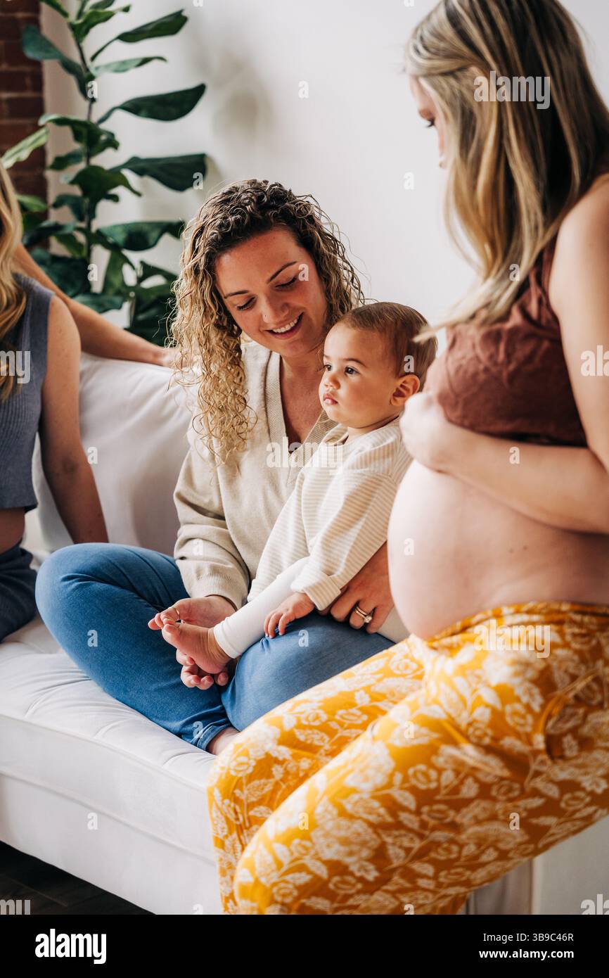 Femme enceinte et amis se réunissent avec le tout-petit sur un canapé blanc confortable Banque D'Images
