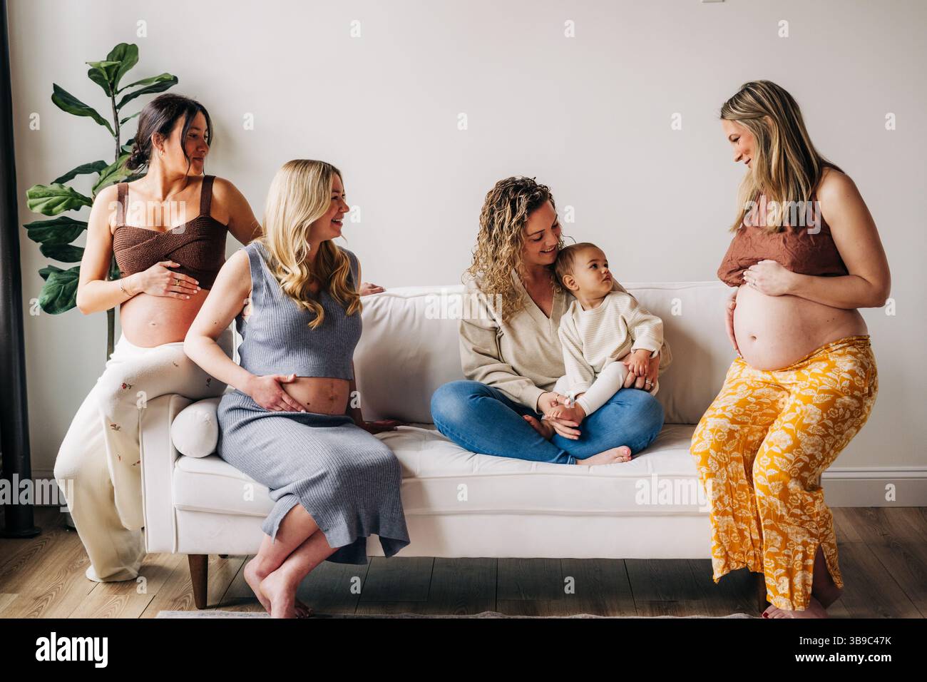 Trois femmes enceintes et mère avec un enfant assis sur un canapé blanc Banque D'Images