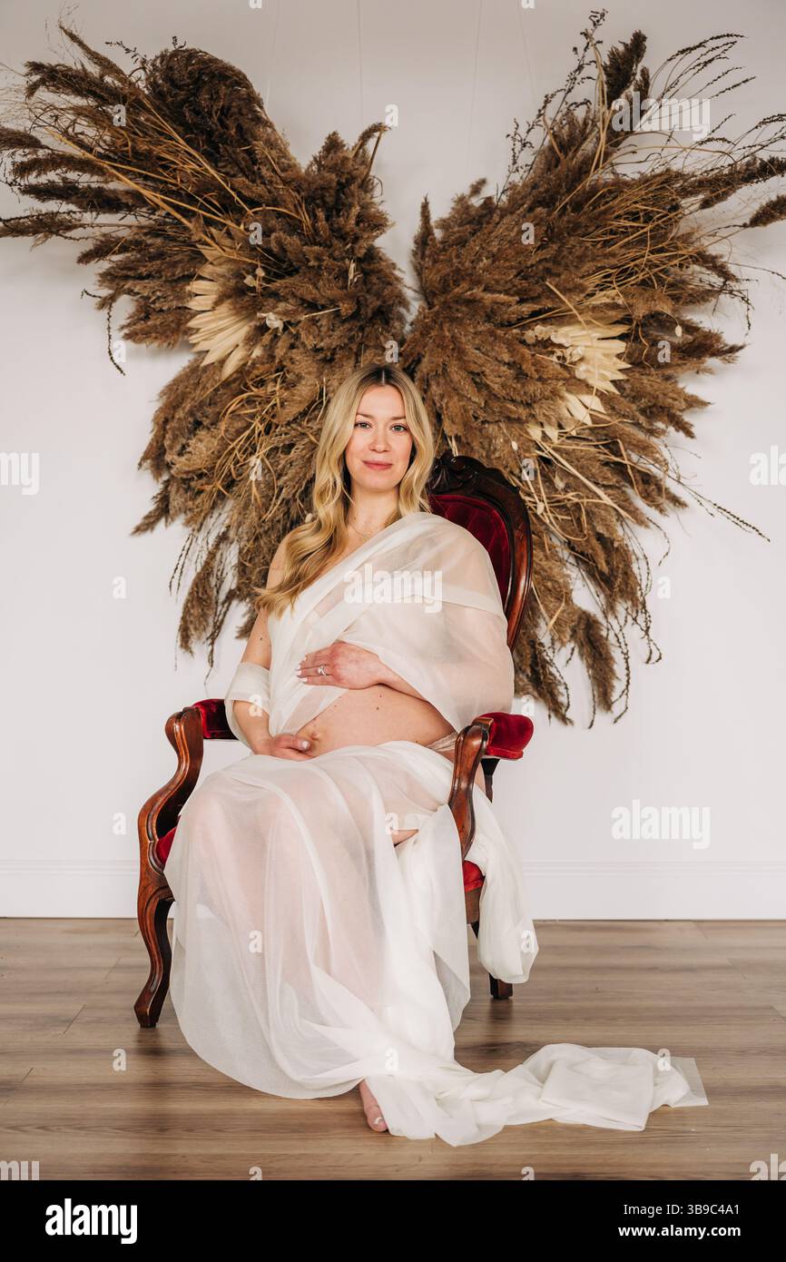Femme enceinte en robe pure s'assoit calmement avec des ailes d'ange pampas Banque D'Images