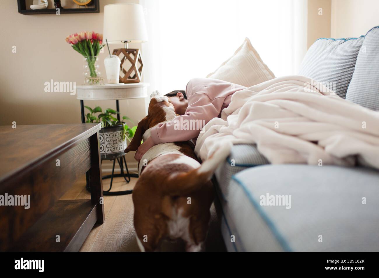 Adolescent embrassant le chien de basset tout en étant allongé sur le canapé sous une couverture douce Banque D'Images