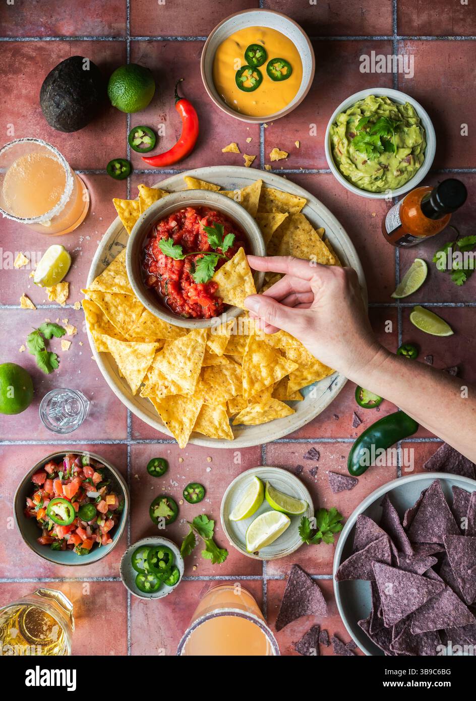 Vue de dessus main trempette dans la salsa avec guacamole, boissons sur carrelage. Banque D'Images