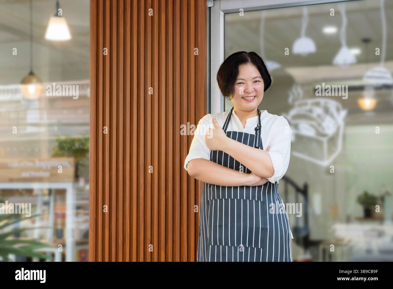 concept réussi de propriétaire de petite entreprise. Une femme asiatique confiante portant un tablier, debout avec ses pouces vers le haut avec le visage souriant devant la boulangerie Banque D'Images