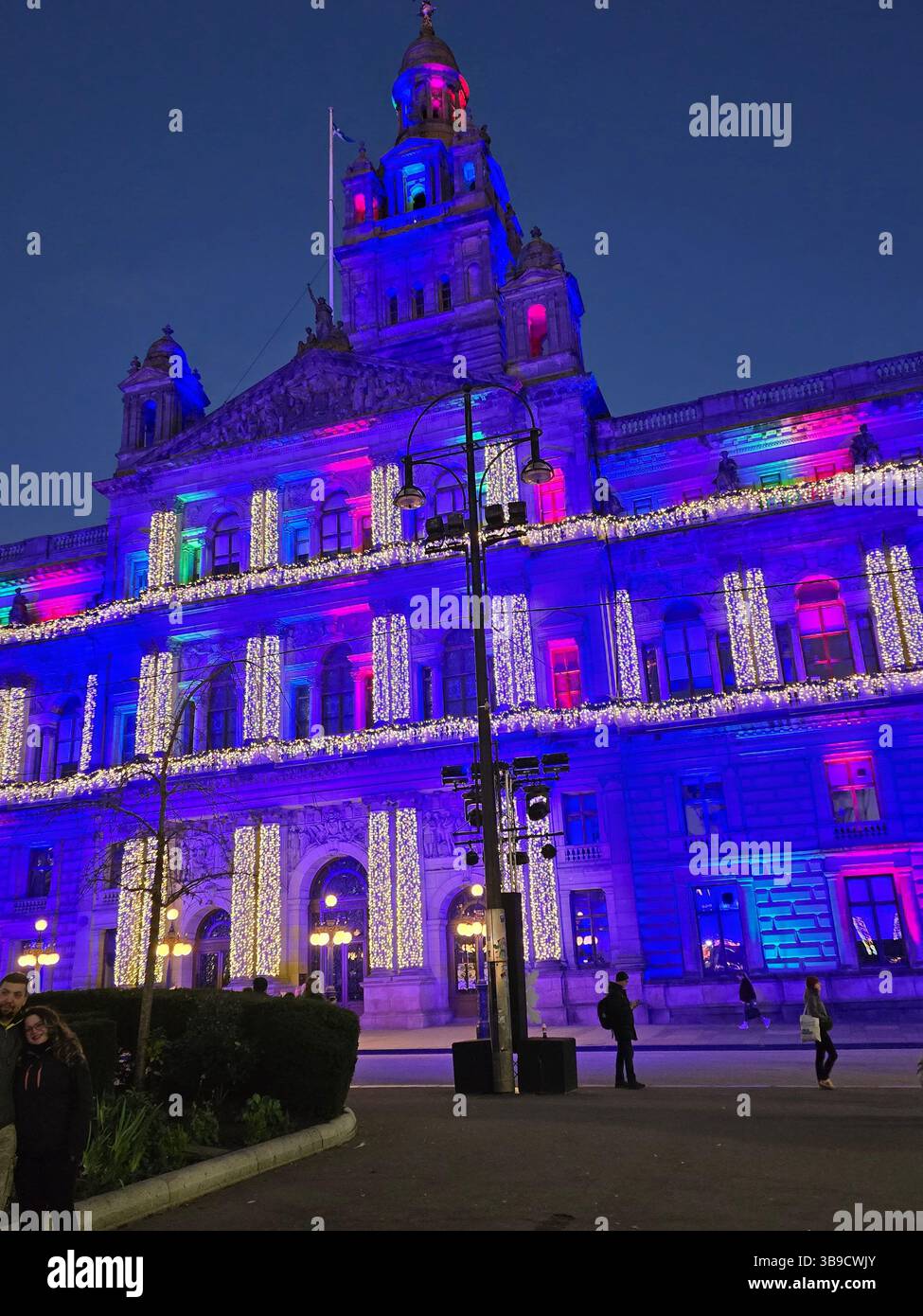 Le City Chambers éblouit avec un éclairage festif bleu, violet et rose vif pendant la saison de Noël. Une scène animée qui se déroule alors que les gens se promènent. Banque D'Images