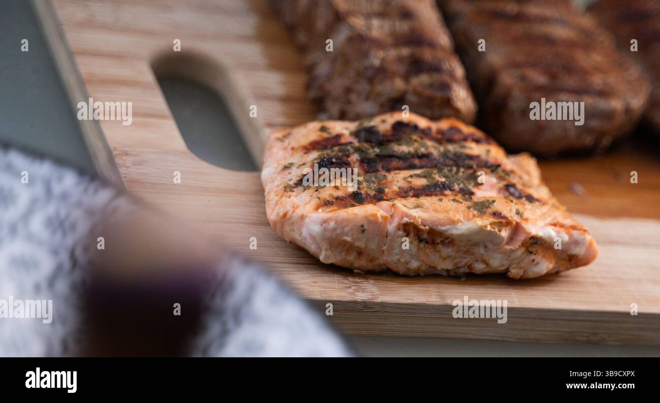 Une délicieuse tartinade de saumon et de viande grillés, mettant en valeur des couleurs et des textures vibrantes sur une planche de bois. Banque D'Images