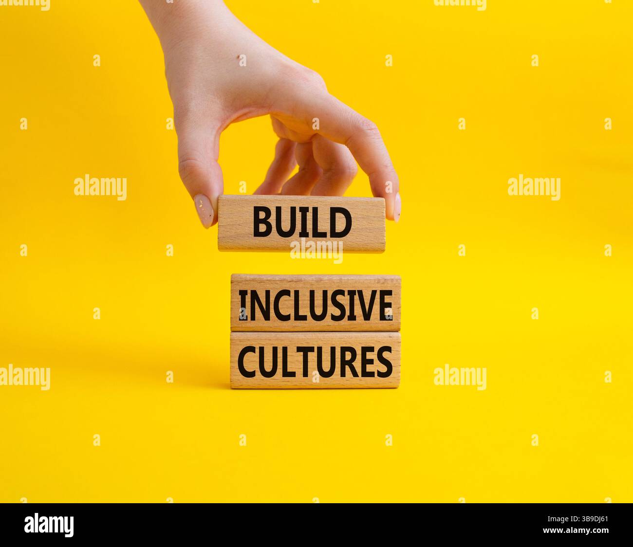 Symbole construire des cultures inclusives. Les blocs de bois avec des mots construisent des cultures inclusives. Beau fond jaune. Main d'homme d'affaires. Affaires et construction Banque D'Images