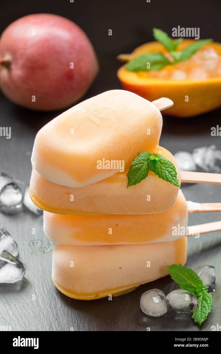 Colonne de 4 sundae sorbet à la mangue mélanger la crème glacée derrière la mangue et la mangue coupée près des glaçons sur un fond noir. Sorbet à la mangue sundae mix popsicles à la crème glacée. Vertical. Banque D'Images
