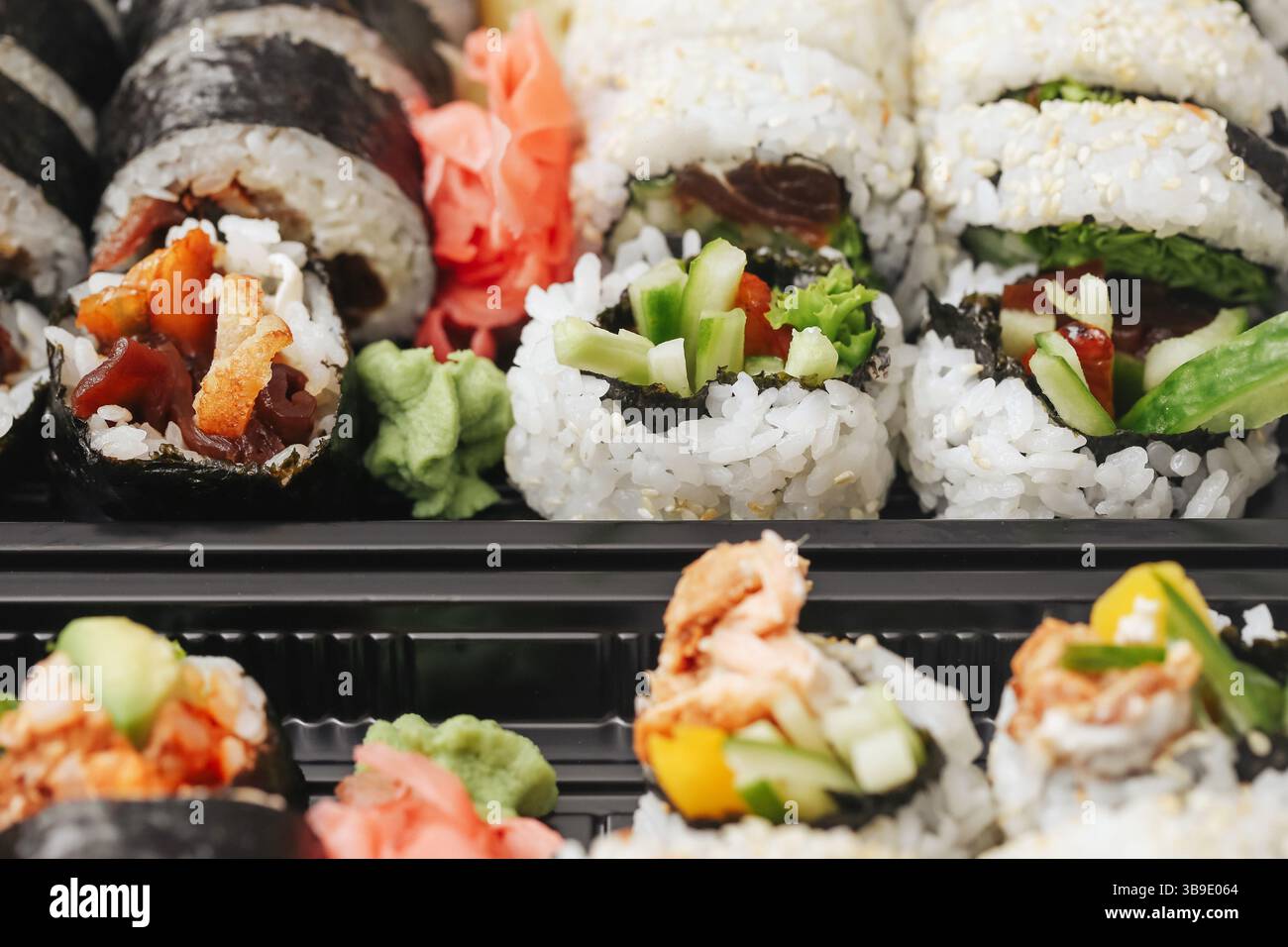 Petits pains de sushi frais en gros plan. Cuisine japonaise à emporter. Riz savoureux avec du poisson et des légumes. Wasabi et gingembre servis. Déjeuner asiatique dans une boîte en plastique. Banque D'Images