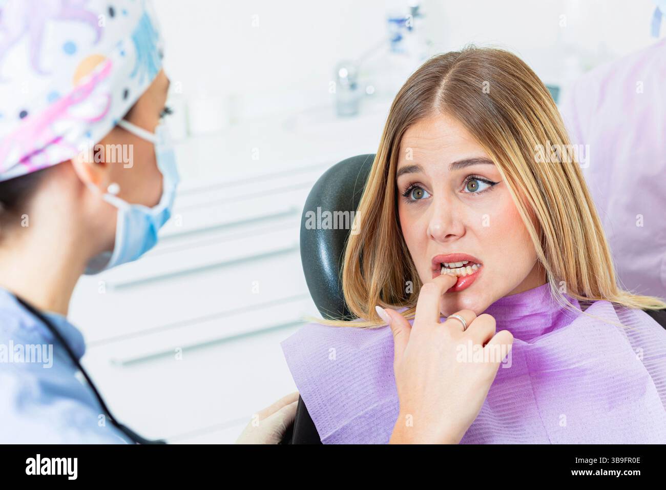 Jeune femme montrant ses dents pendant un examen dentaire dans une clinique, exprimant son inquiétude et son anxiété au sujet de sa santé buccodentaire Banque D'Images