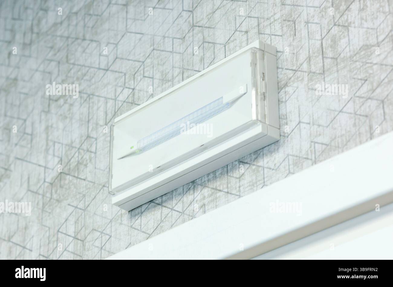 Luminaire de secours blanc monté sur un mur à motifs, éclairant la zone et servant de mesure de sécurité pendant les pannes de courant, assurant la visibilité et le guidage dans les situations critiques Banque D'Images