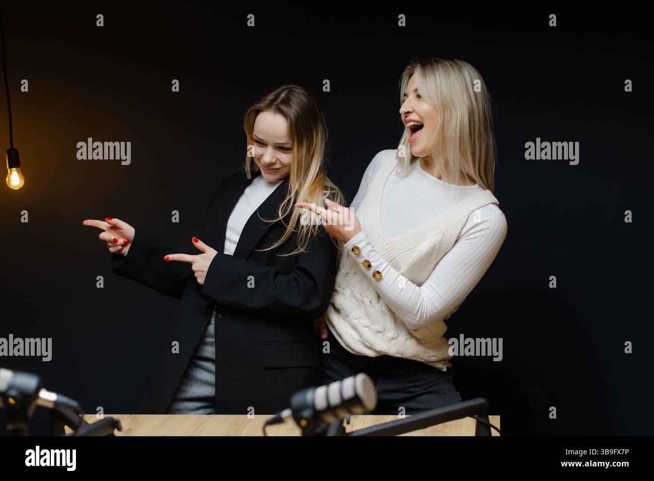 Deux podcasters féminins pointent et rient lors d'une session d'enregistrement dans un studio professionnel, créant un contenu audio attrayant Banque D'Images