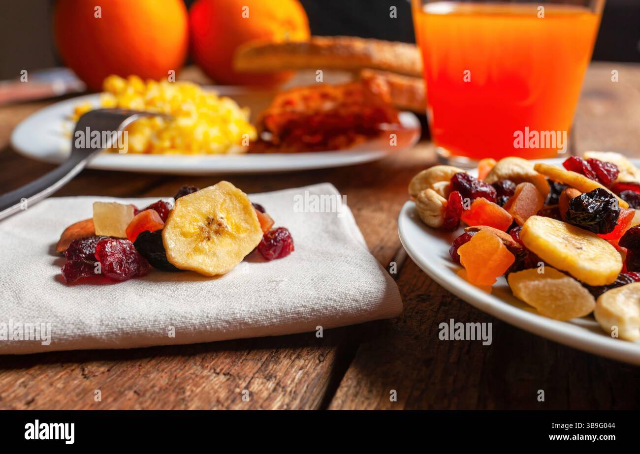 Mélange de fruits secs, jus d'orange rafraîchissant et œufs brouillés moelleux créant un petit déjeuner vibrant et nutritif sur une table en bois rustique, parfait pour les matins énergisants Banque D'Images