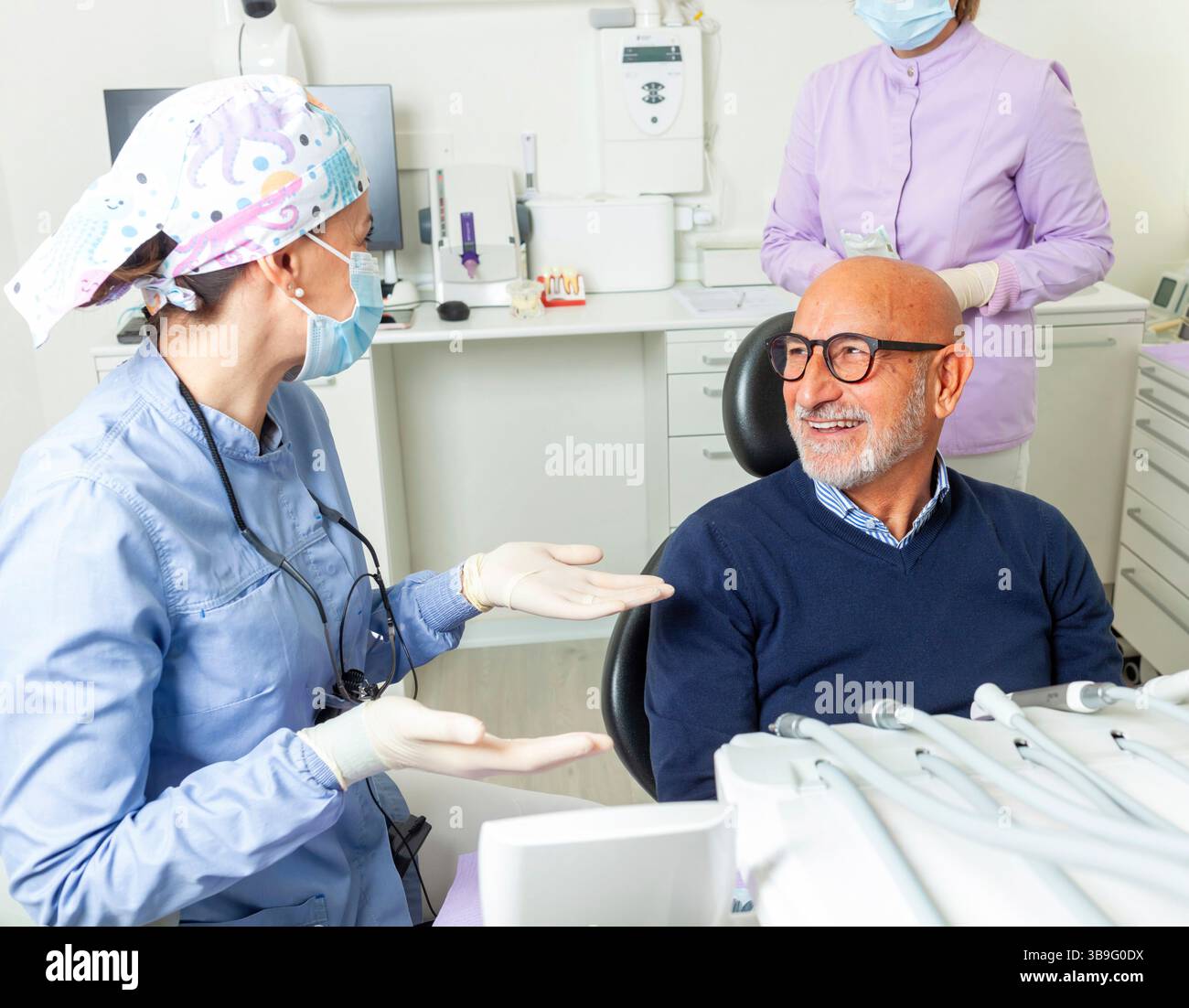 Dentiste femme portant un masque chirurgical expliquant le traitement à un homme âgé souriant assis dans le fauteuil dentiste dans la clinique dentaire Bright Banque D'Images