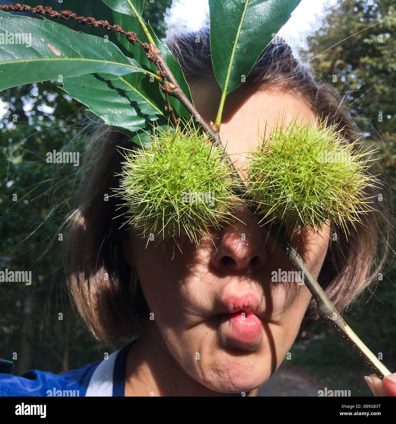 Jeune femme couvrant ses yeux avec deux boîtiers extérieurs verts fermés de châtaignes, tout en faisant une expression drôle de visage. Amusement dans la forêt d'automne Banque D'Images