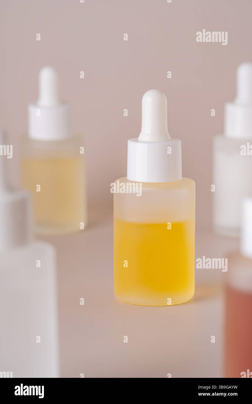 Une collection de différents flacons compte-gouttes remplis de liquides jaunes et clairs disposés sur un fond beige doux, incarnant un minimalis propre et minimalis Banque D'Images
