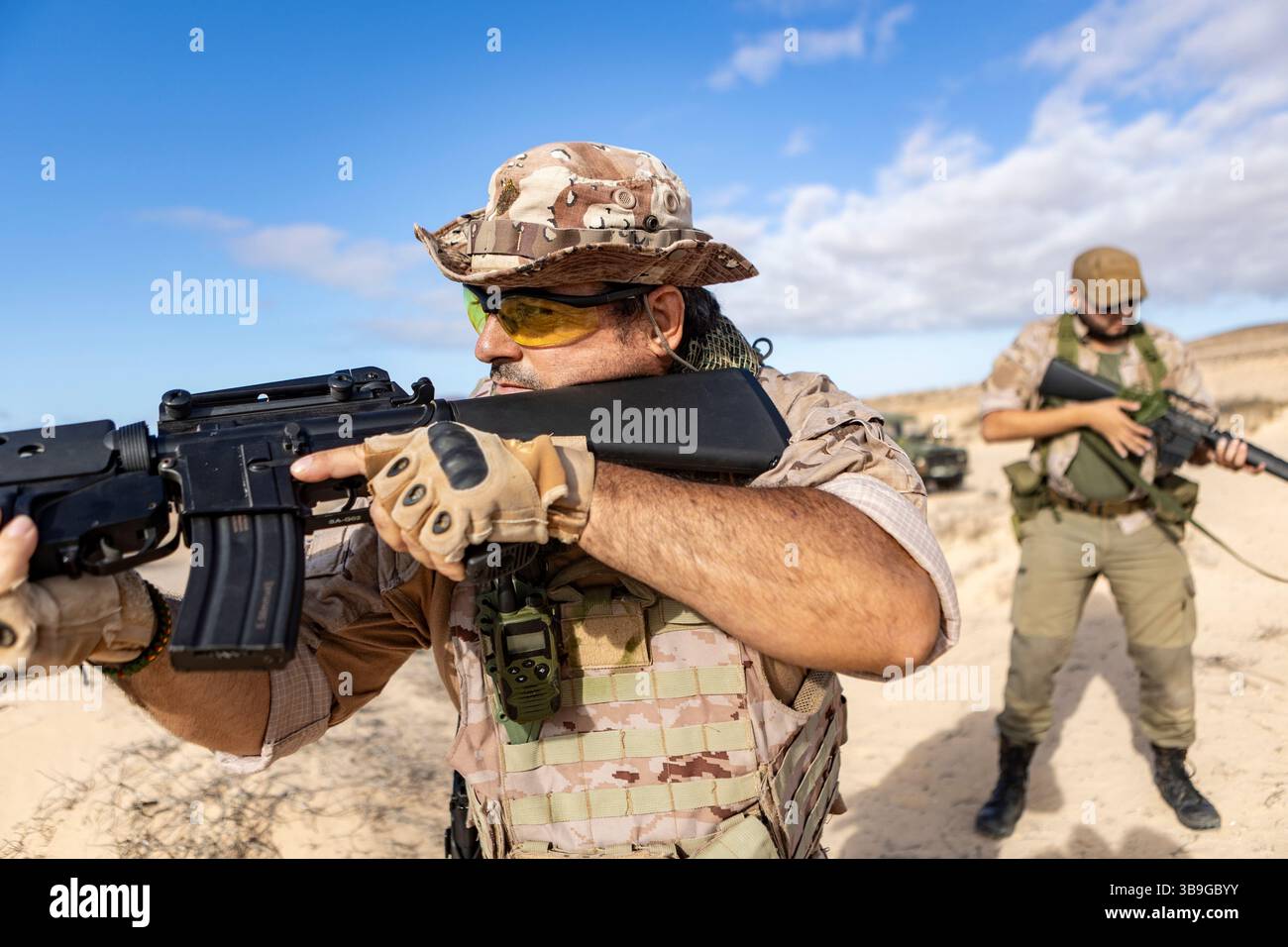 Deux soldats en équipement tactique participent à un exercice d'entraînement dans un cadre désertique. Ils sont concentrés et tiennent des fusils, démontrant leur disponibilité militaire Banque D'Images