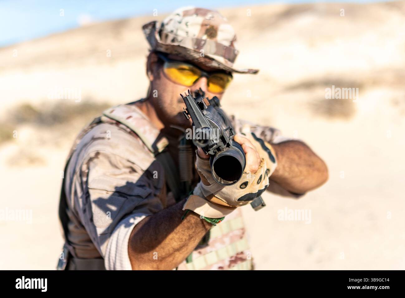 Un soldat en équipement de combat tactique vise une arme à feu dans un cadre désertique. L'accent est mis sur l'armée, la stratégie et l'état de préparation, mettant en évidence la guerre moderne e Banque D'Images
