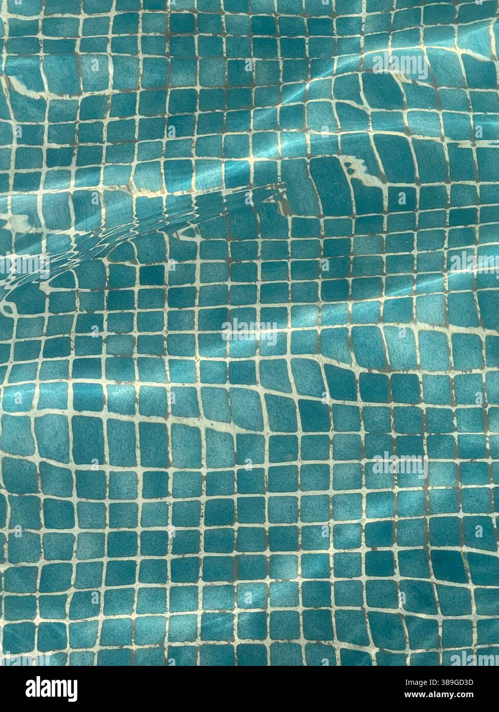 Une vue sereine sur la surface carrelée bleue d'une piscine, avec la lumière du soleil créant des ondulations et des reflets doux. Le mouvement de l'eau ajoute un texte apaisant Banque D'Images