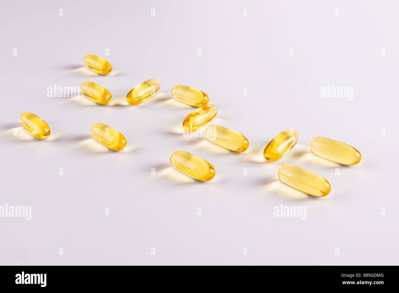 Gros plan des gélules d'oméga 3 et de vitamine E sur fond blanc. Les capsules jaunes brillantes sont dispersées, soulignant leur texture translucide Banque D'Images