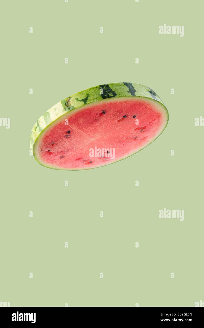 Tranche de pastèque fraîche planant sur un fond vert pastel minimaliste, incarnant les vibrations estivales et une alimentation saine Banque D'Images