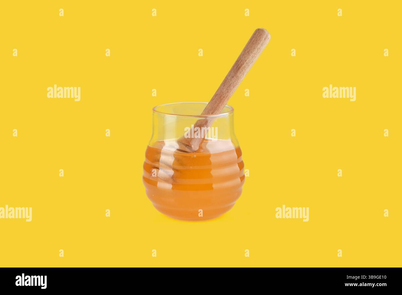 Miel s'égouttant de la trempette en bois dans le bocal en verre sur fond jaune, représentant l'édulcorant naturel et la nourriture saine Banque D'Images