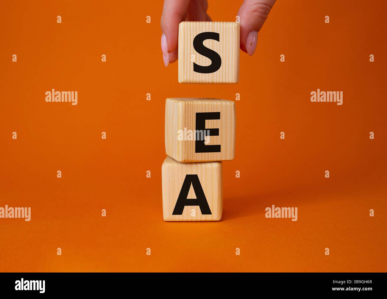 SEA - symbole publicitaire des moteurs de recherche. Cubes en bois avec les mots MER. Main d'homme d'affaires. Beau fond orange. Concept d'affaires et DE MER. Copier spa Banque D'Images