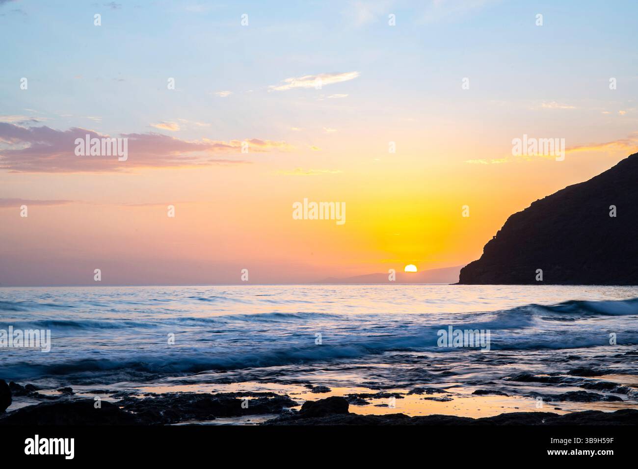 Coucher de soleil dans une baie. Beau paysage photographié avec une vue sur une côte aride à marée basse. À une lumière calima, sable du désert au crépuscule avec une grande couleur de ciel à Gran Tarajal, îles Canaries, Fuerteventura, Espagne Banque D'Images
