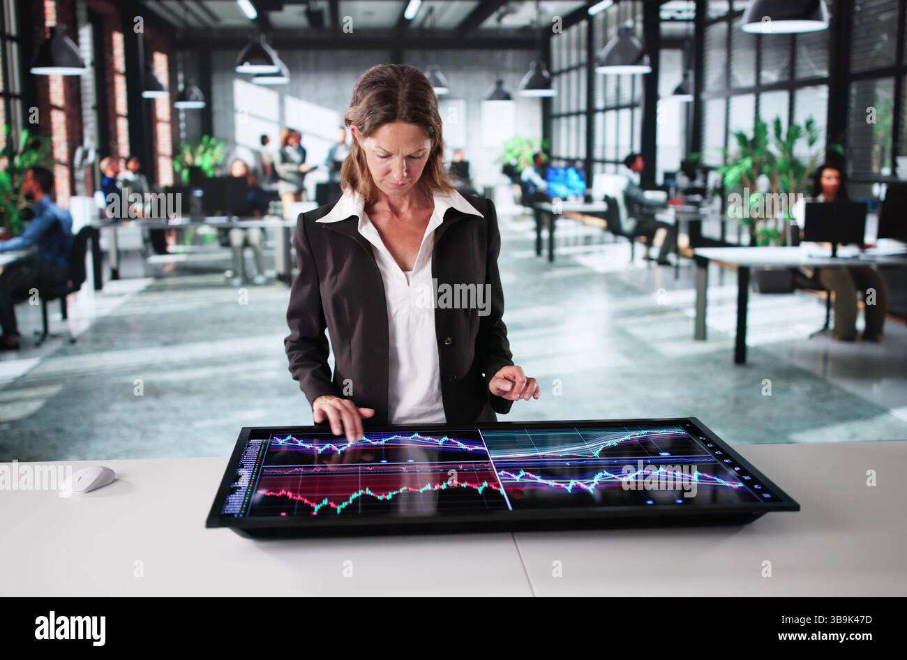 Femme d'affaires mature surveille le marché boursier en ligne dans le cadre de bureau. Banque D'Images
