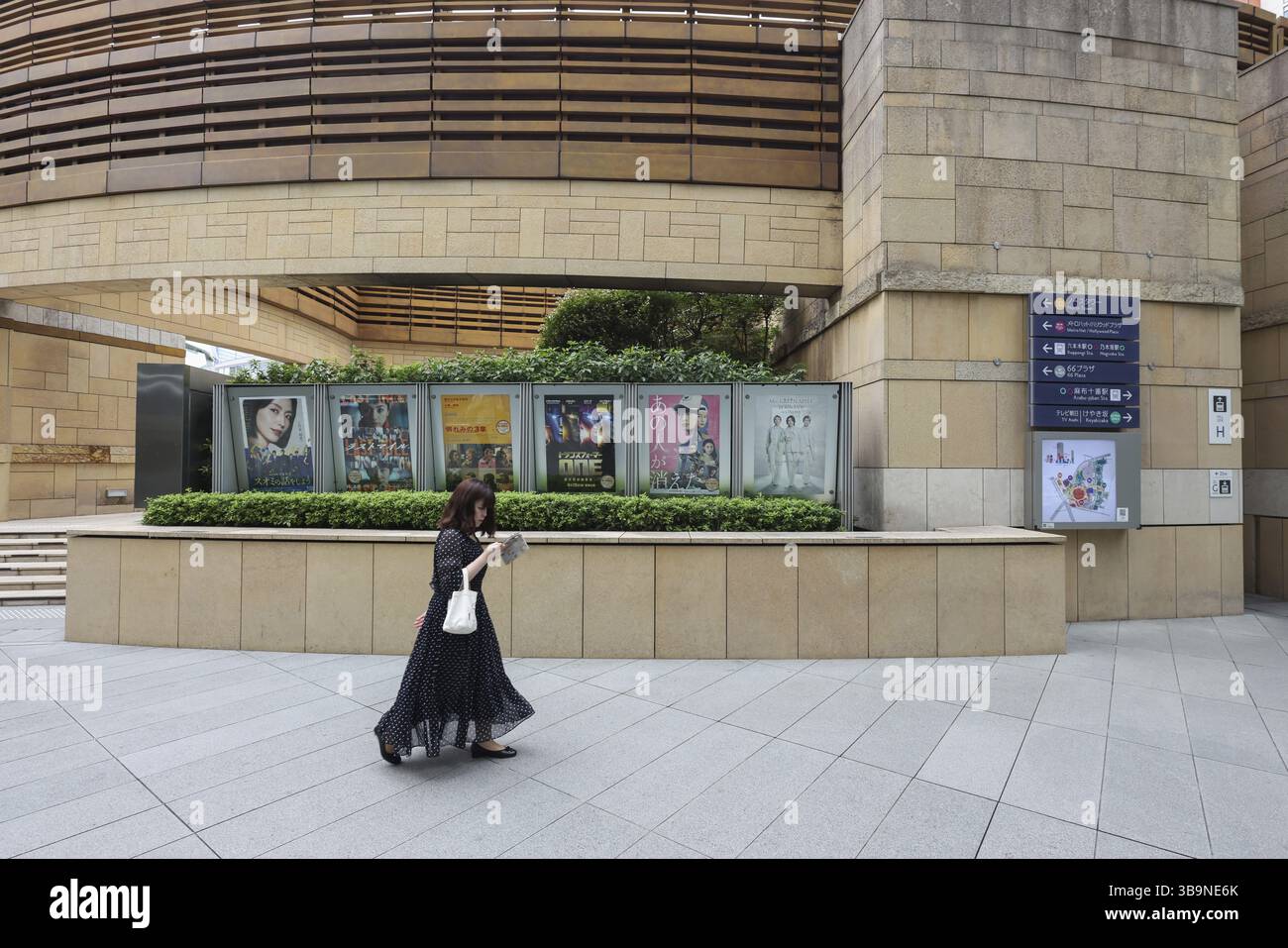 Femme utilisant un téléphone portable marchant devant des affiches de film dans le complexe commercial et de bureaux de Roppongi Hills, Tokyo, Japon, Asie Banque D'Images