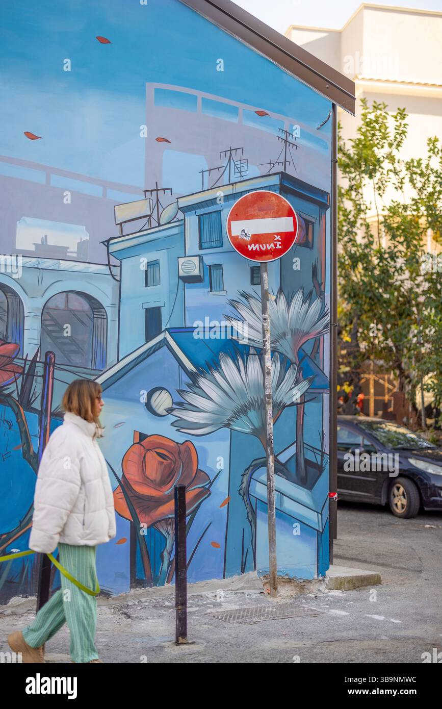 Une femme promène son chien blanc devant une murale de rue vivante dans un quartier romain créatif, mêlant art urbain et moments quotidiens Banque D'Images