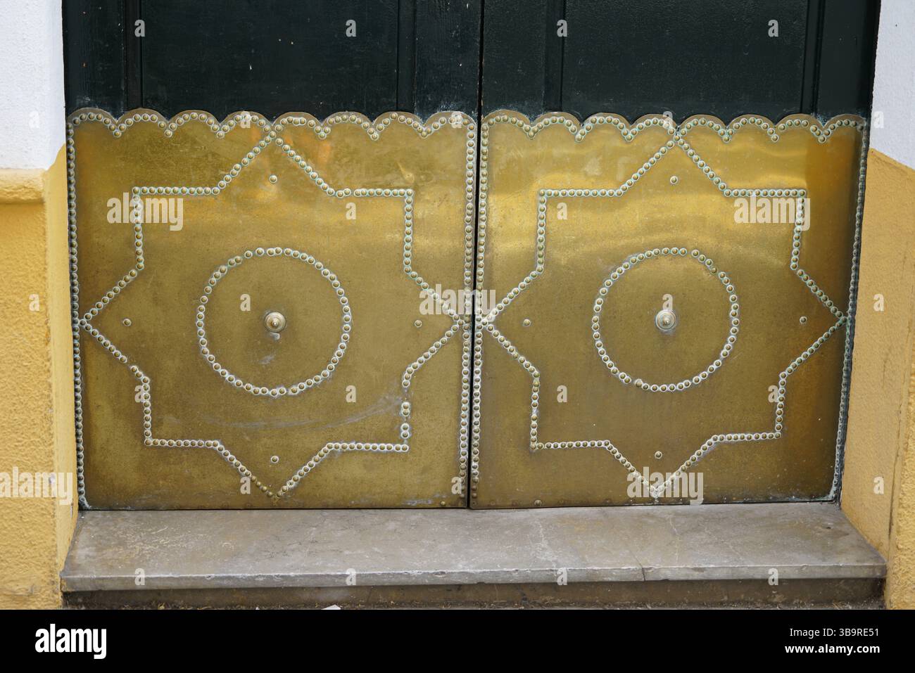 Panneaux de porte en métal cloutés traditionnels avec décoration géométrique et patine sur une entrée de bâtiment à Séville, Espagne, montrant classique Banque D'Images