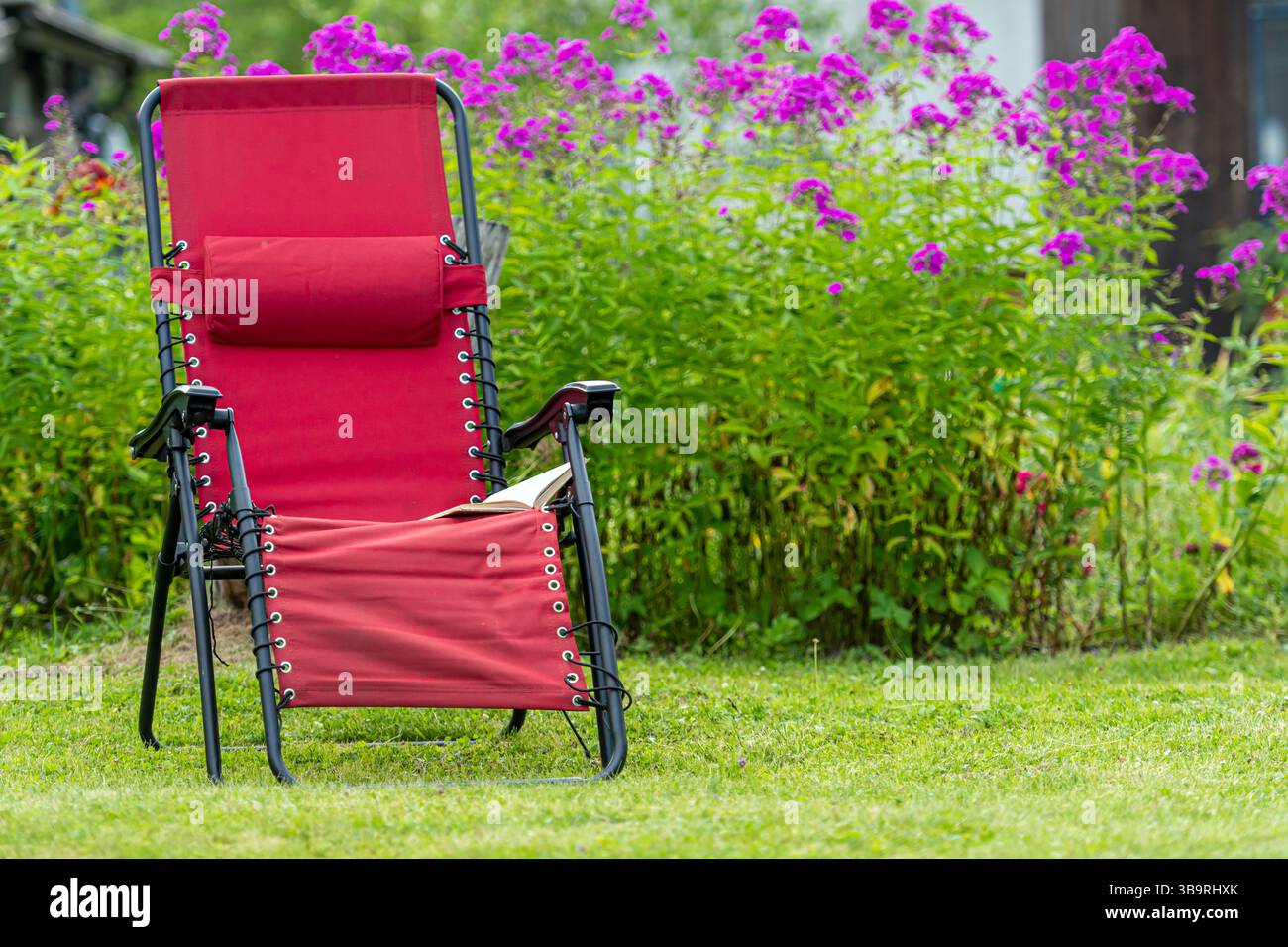 Une chaise confortable se trouve dans un jardin animé rempli de fleurs en fleurs par une journée ensoleillée. Banque D'Images
